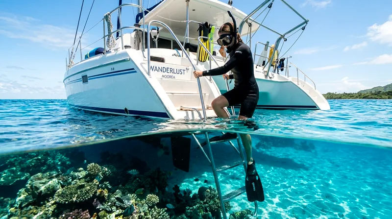 Snorkeler entering water from catamaran's swim platform at reef site
